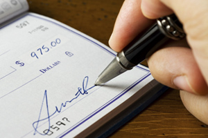 Close up of a hand signing a check. Please note that the signature is fictitious.