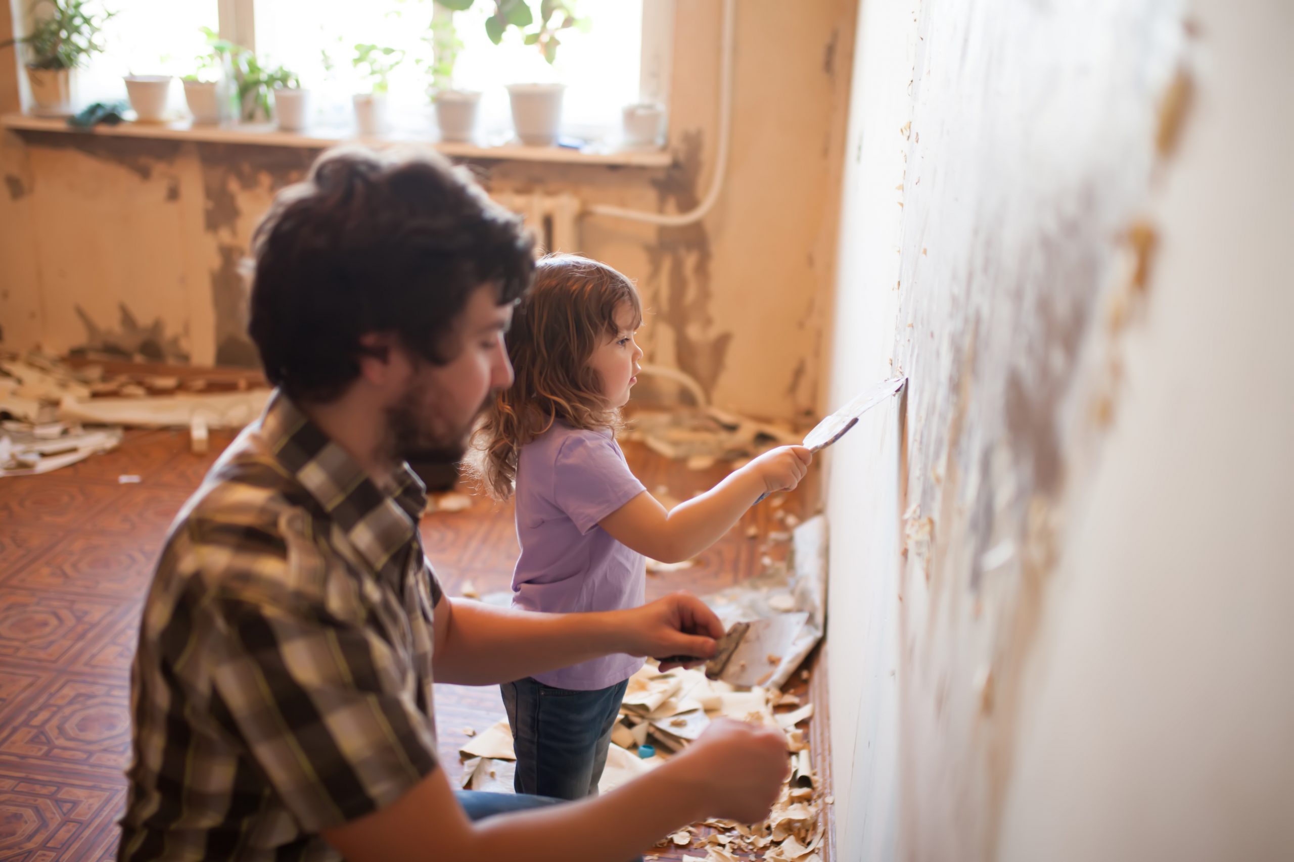 Father and daughter repairing wall using putty knives. Learn about taking out a personal loan for home improvement projects.