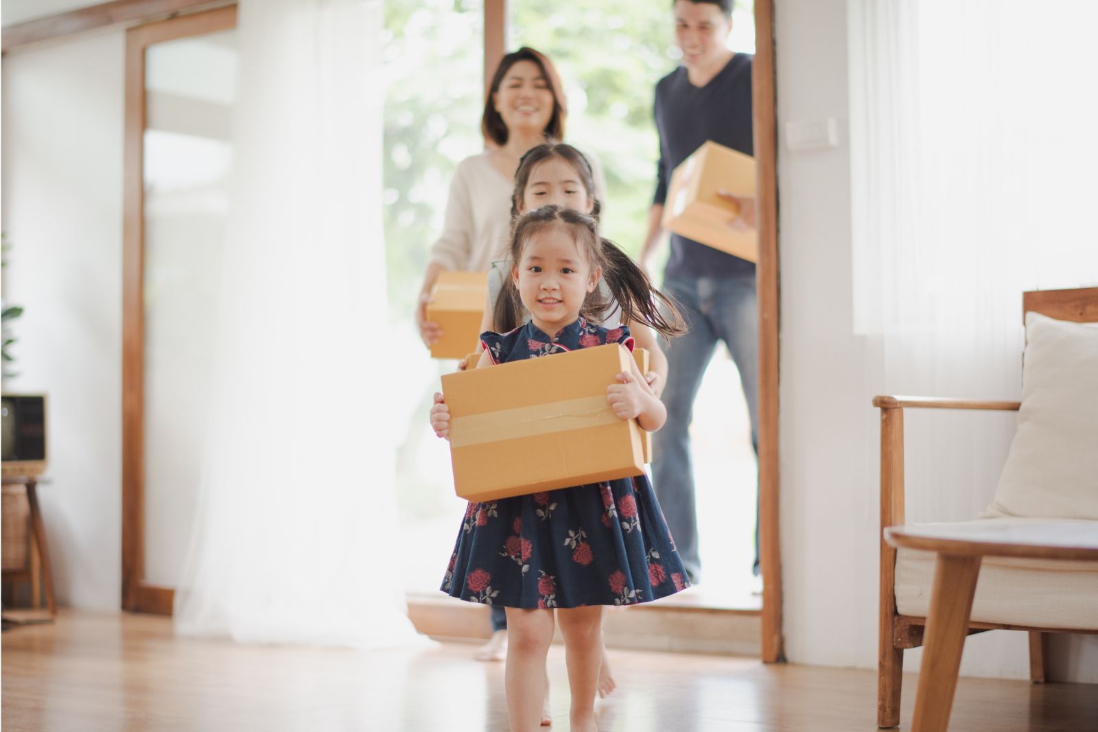 family smiles carrying boxes into new home.